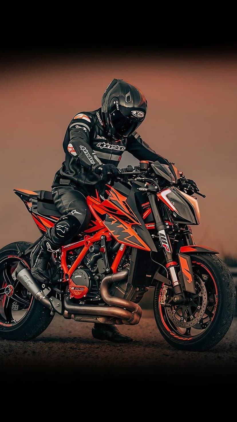 Motorcyclist in black leather gear sits on an orange KTM bike during a warm sunset with a blurred background.