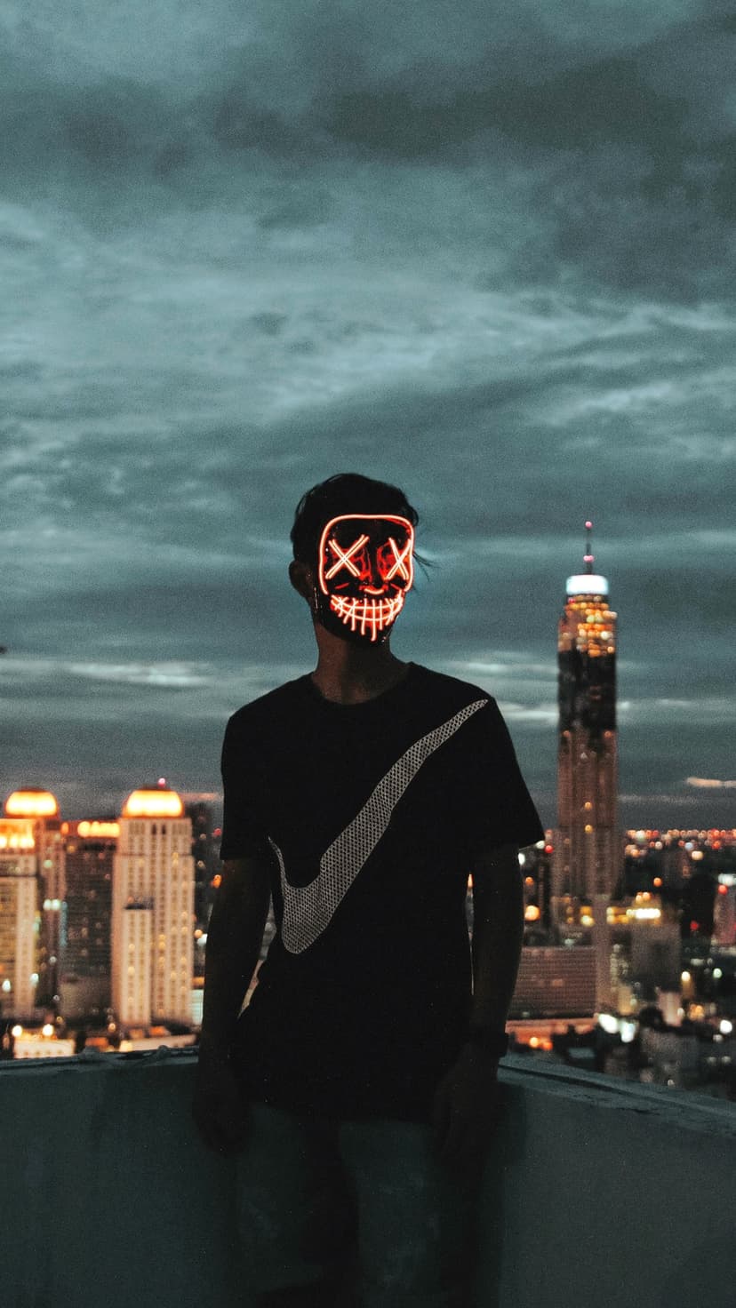 Masked figure with glowing red X eyes overlooks a night cityscape with lit skyscrapers and dark clouds.