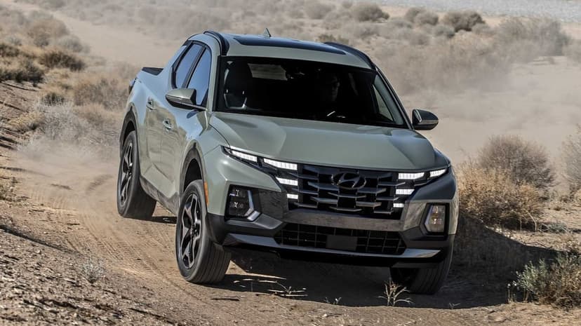Sage green Hyundai Santa Cruz pickup truck driving on a dusty desert trail under bright natural daylight.