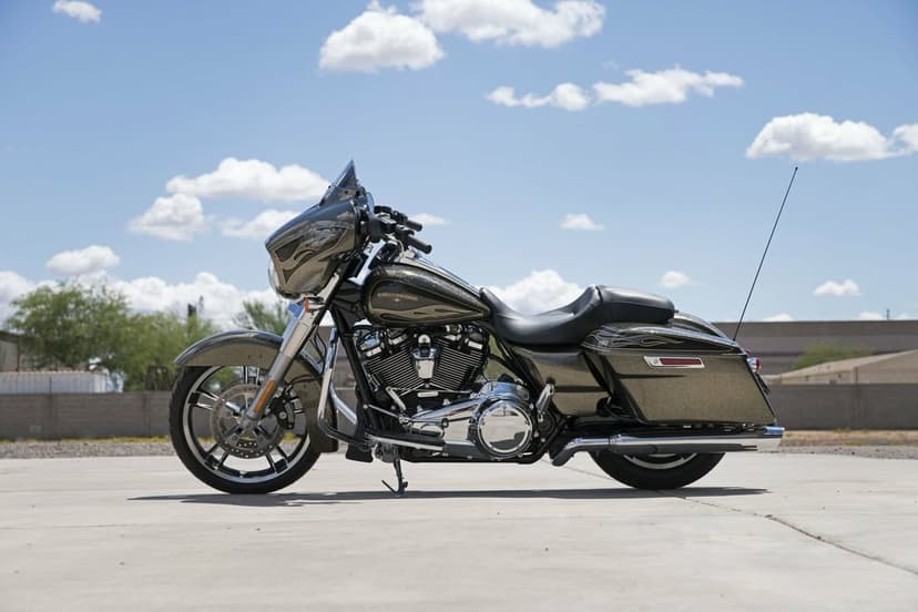 Gold metallic Harley-Davidson cruiser with black flames on a concrete lot under a blue cloudy sky.