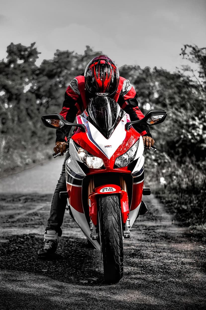 Professional racer in red leathers sits on a sportbike against a blurred grey-tone forest backdrop.