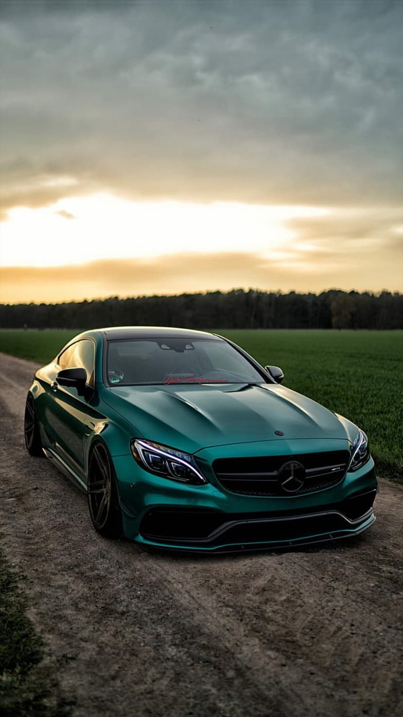 Mercedes-AMG C63 Coupe in emerald green parked on a dirt trail under a dramatic sunset sky with dark alloy wheels