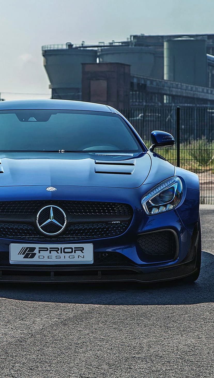 Blue Mercedes-AMG GT with Prior Design wide-body kit and vertical grille parked on gritty industrial asphalt.