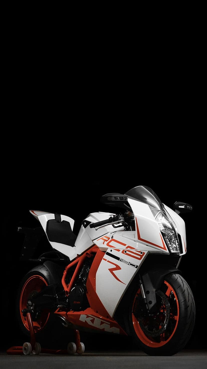 White KTM RC8 motorcycle with orange accents against a black background featuring sharp headlights and alloy wheels.