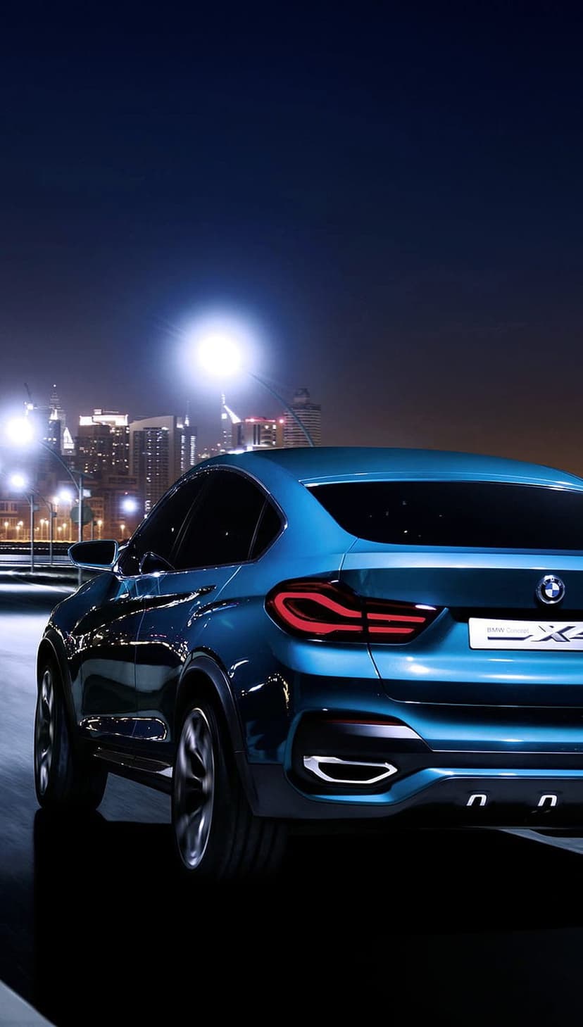 Blue BMW X4 coupe with glowing red taillights driving past illuminated skyscrapers in a night city scene.