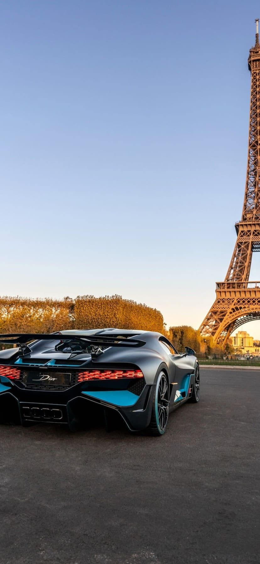Matte grey Bugatti Divo with blue accents parked near the Eiffel Tower in Paris under a clear blue sky.