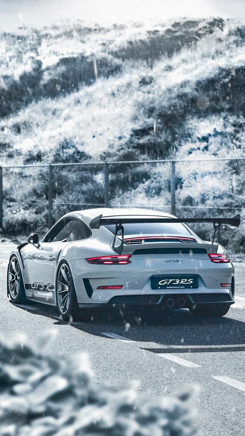 White Porsche GT3 RS with a rear wing driving on a snow-covered road through a blurred winter forest landscape.