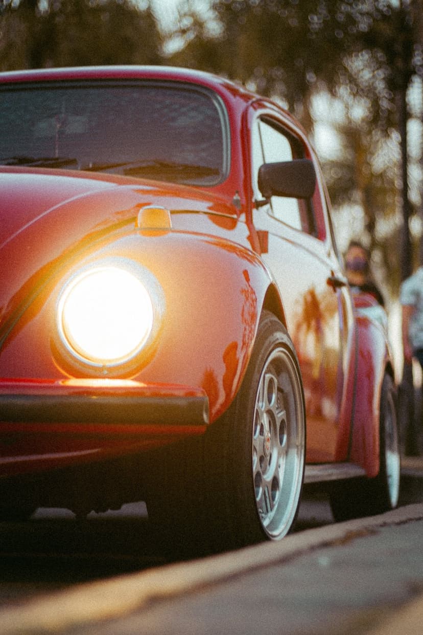 Red classic Volkswagen Beetle with an illuminated round headlight, custom rims, and polished paintwork.