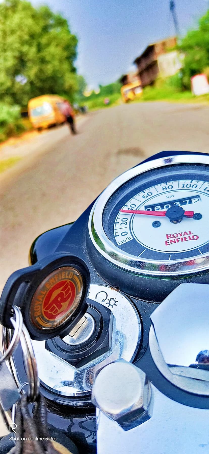Royal Enfield motorcycle speedometer with a red needle and chrome bezel against a blurred green outdoor background.