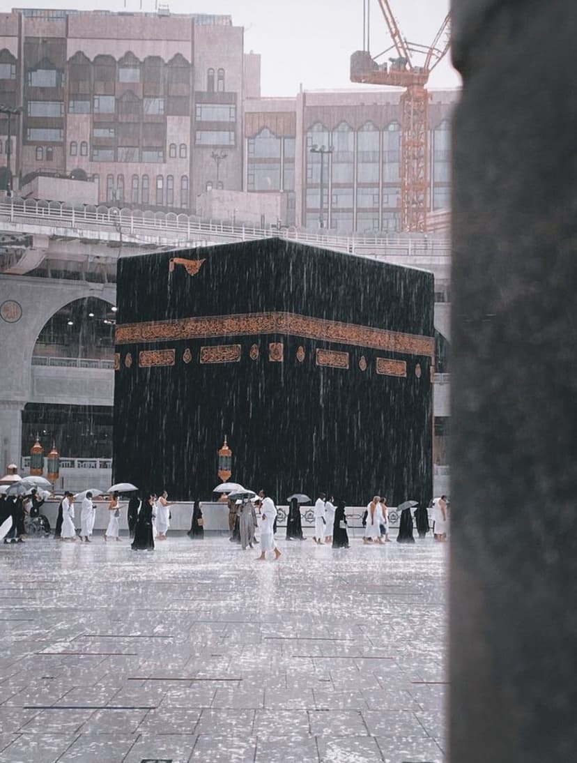 Kaaba cube in Mecca during a rainstorm with pilgrims holding umbrellas on a wet, reflective marble courtyard.