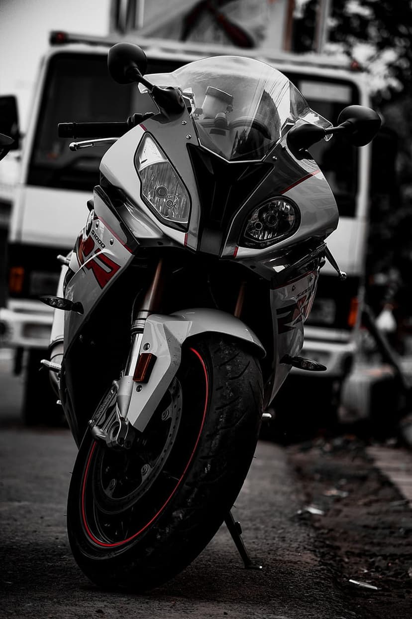 White and red sportbike with glossy fairings parked on a grey asphalt road featuring a soft bokeh background.