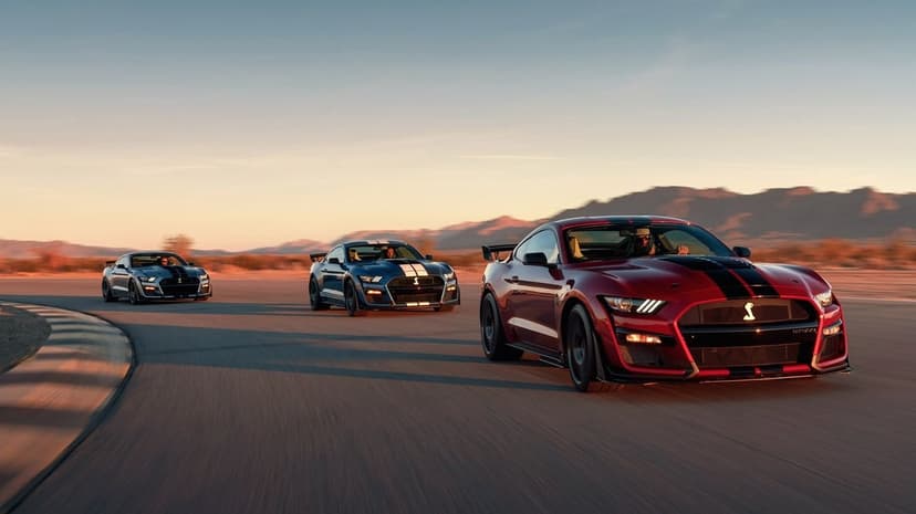Three Ford Mustang Shelby GT500 muscle cars driving on a desert race track during golden hour sunset.
