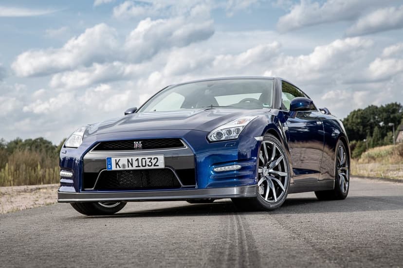 Blue Nissan GT-R R35 parked on a grey asphalt road under a cloudy sky with green trees in the background.