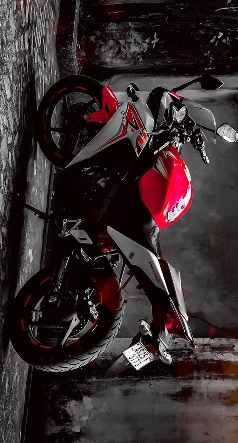 Red and white sport motorcycle with crimson rims parked against a distressed gray concrete wall in dramatic light.