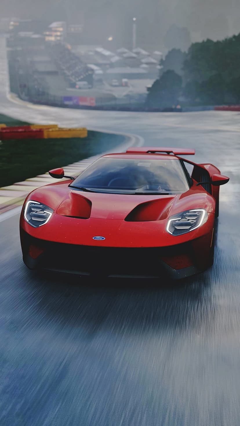 Red Ford GT supercar racing on a wet asphalt track with motion blur and water spray under an overcast sky.