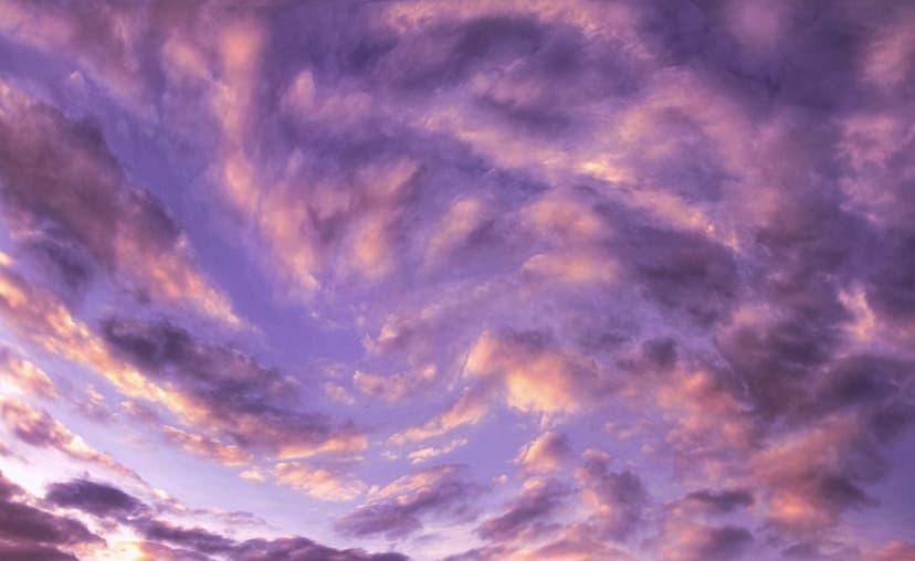 Swirling violet and orange clouds transition across a twilight sky with deep textured shadows and golden light.