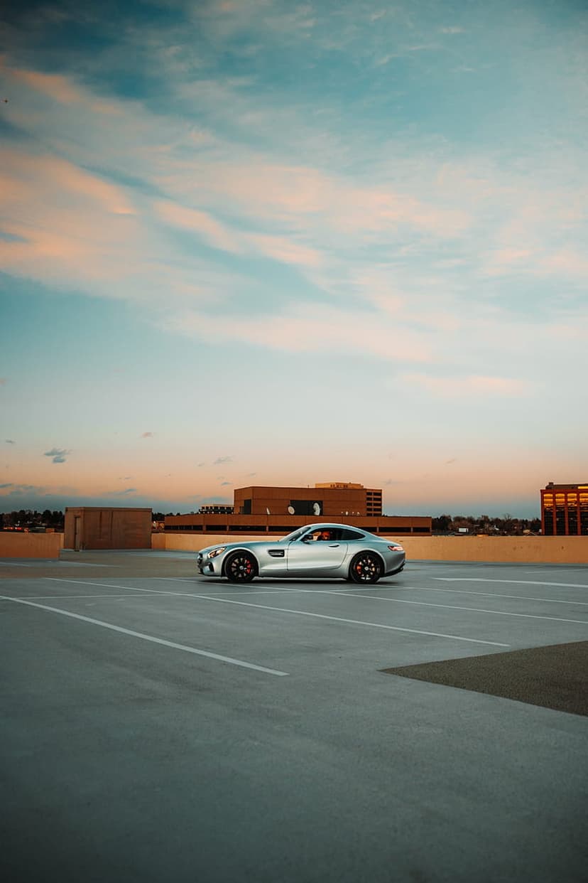 Mercedes-AMG GT S silver coupe parked on a concrete rooftop lot during a vibrant orange and blue sunset.