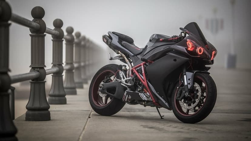 Matte black sportbike with red halo headlights and rims parked on a foggy concrete boardwalk with railings.