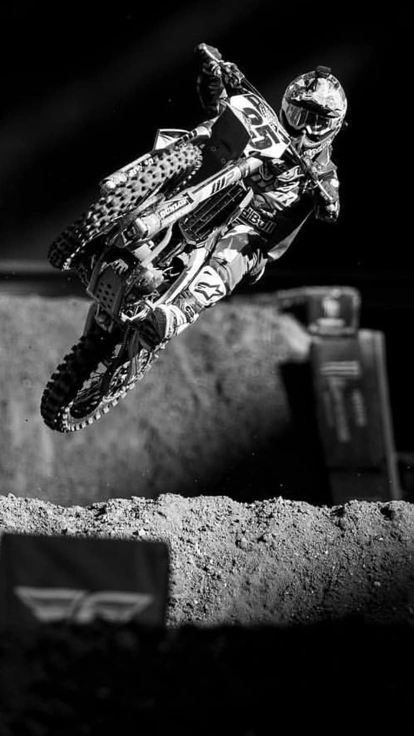 Motocross rider in mid-air performing a jump against a dark background in a grainy black and white photograph.