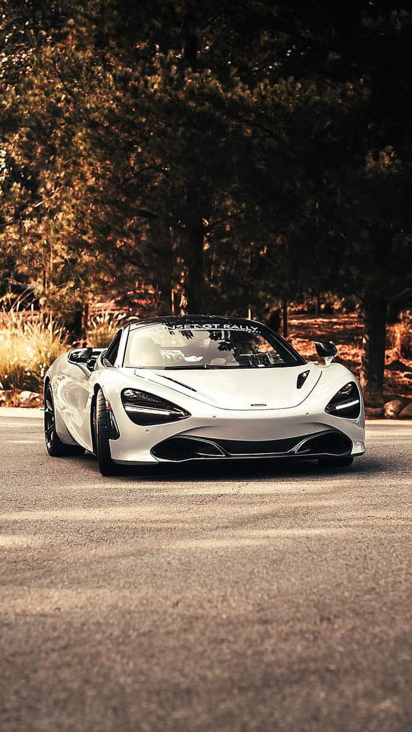 White McLaren 720S convertible on a road with golden autumn trees and sunlit foliage in the background.