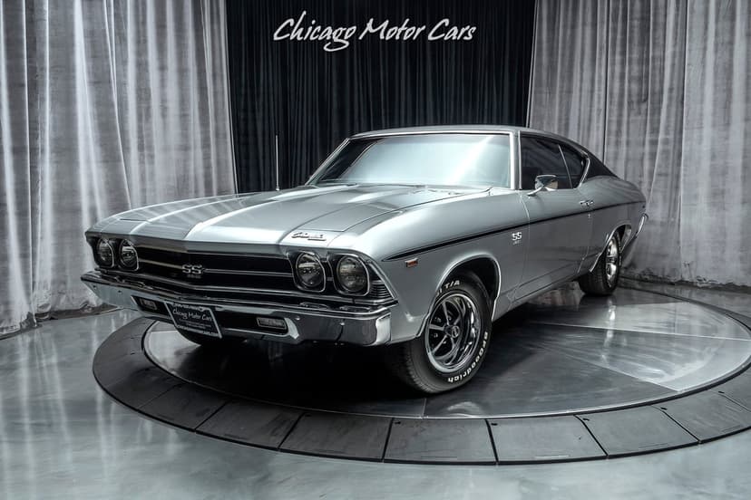 Silver 1969 Chevrolet Chevelle SS on a metal platform with a dark curtain background in a studio.