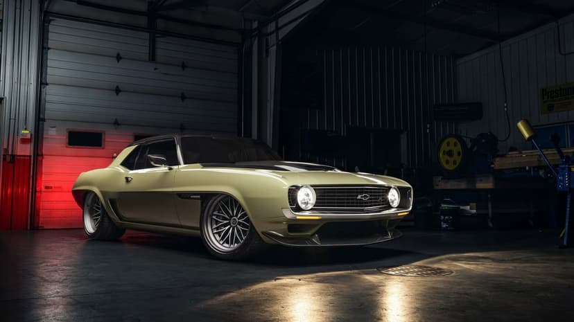 Classic yellow Chevrolet Camaro restomod with carbon fiber trim and custom wheels in a dark garage setting.