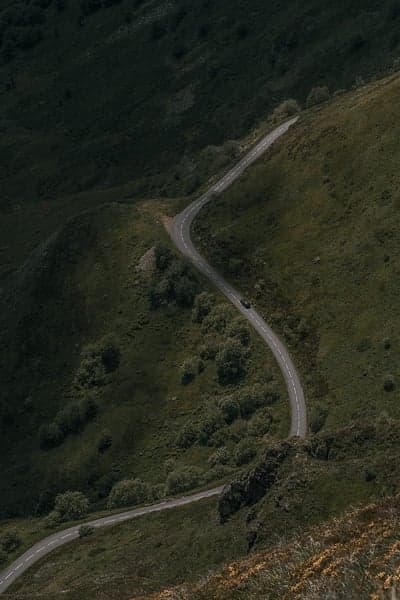 Winding mountain road with a car and scenic green hills