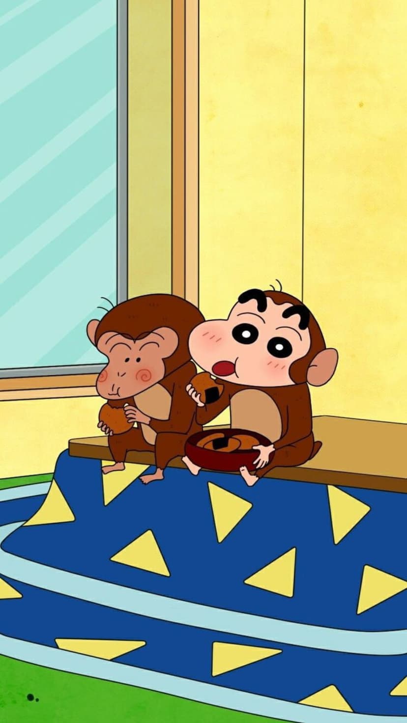 Two monkeys dressed as Shin Chan sit at a patterned table eating snacks inside a sunny yellow room.