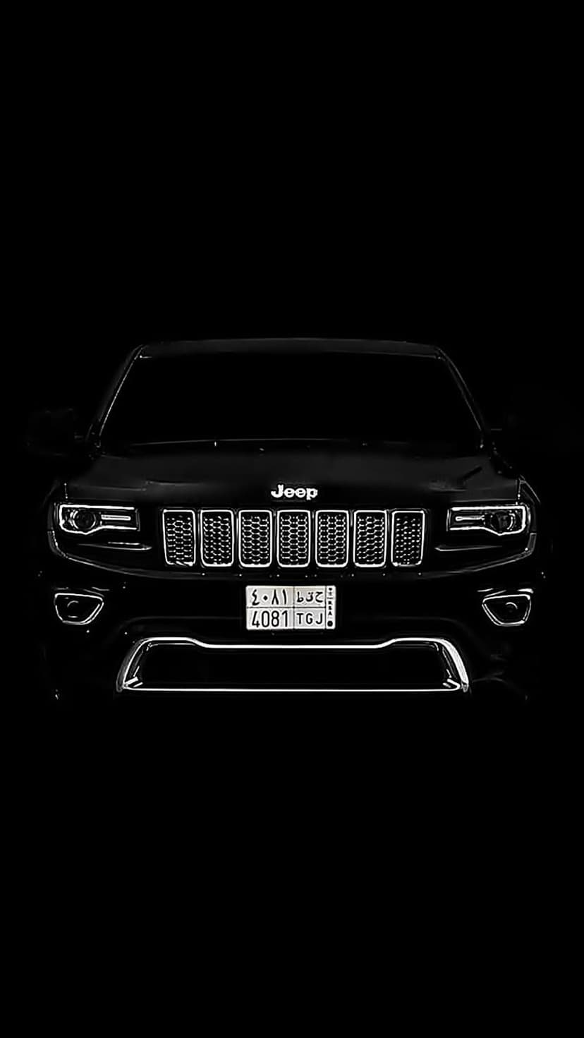 Black Jeep Grand Cherokee front view showing illuminated LED headlights and iconic grille against a dark background.