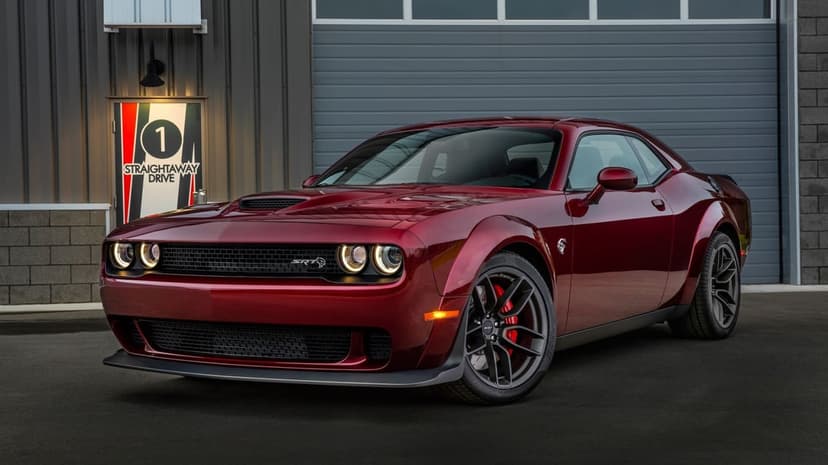 Front view of a dark red Dodge Challenger SRT Hellcat parked in front of a grey industrial garage door.