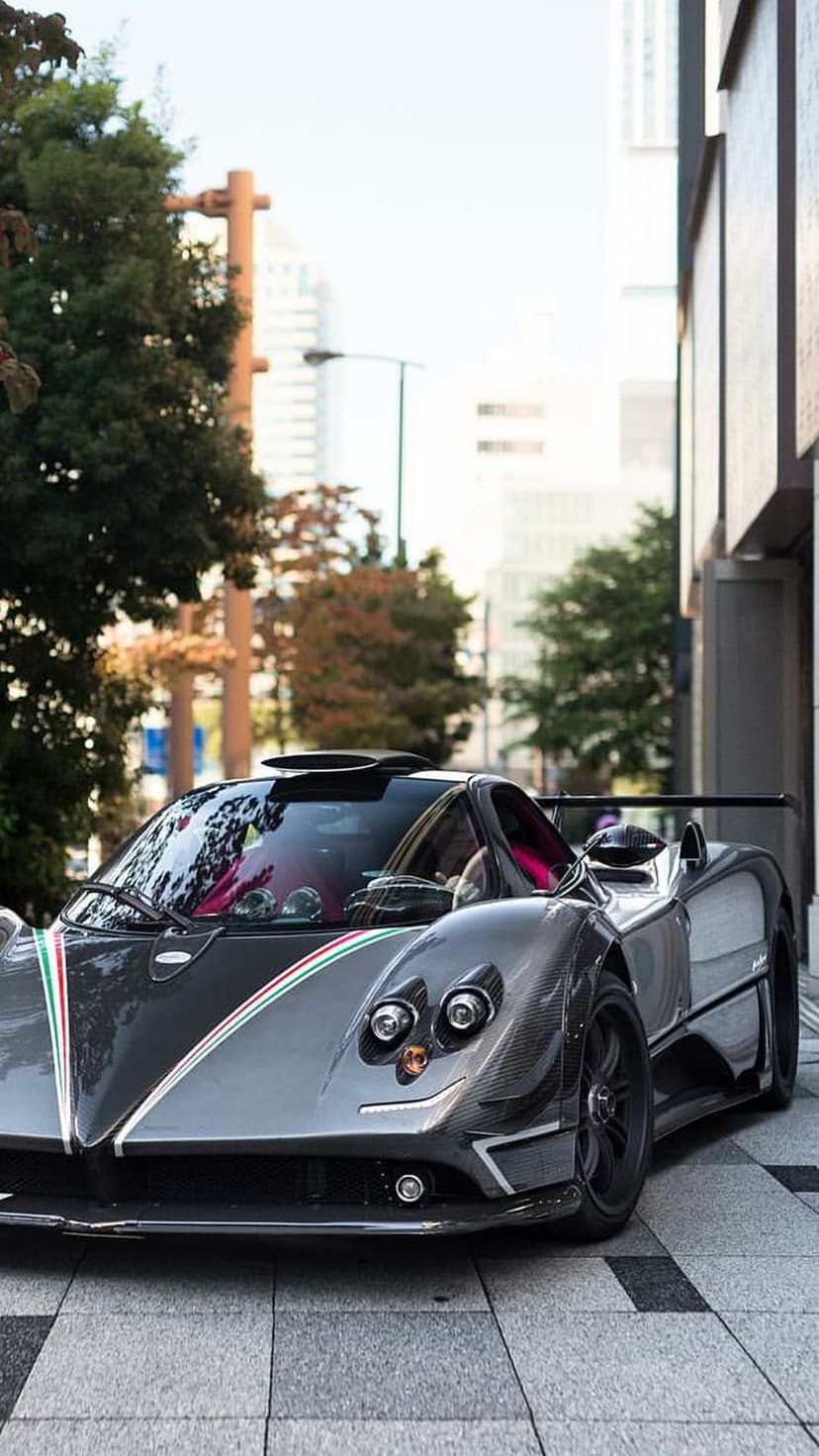 Pagani Zonda Roadster with a pink interior and Italian stripes parked on a city street under tall buildings.