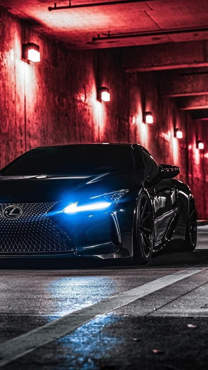 Lexus RC F black sports car with blue headlights in a dark tunnel with red lighting and concrete walls.
