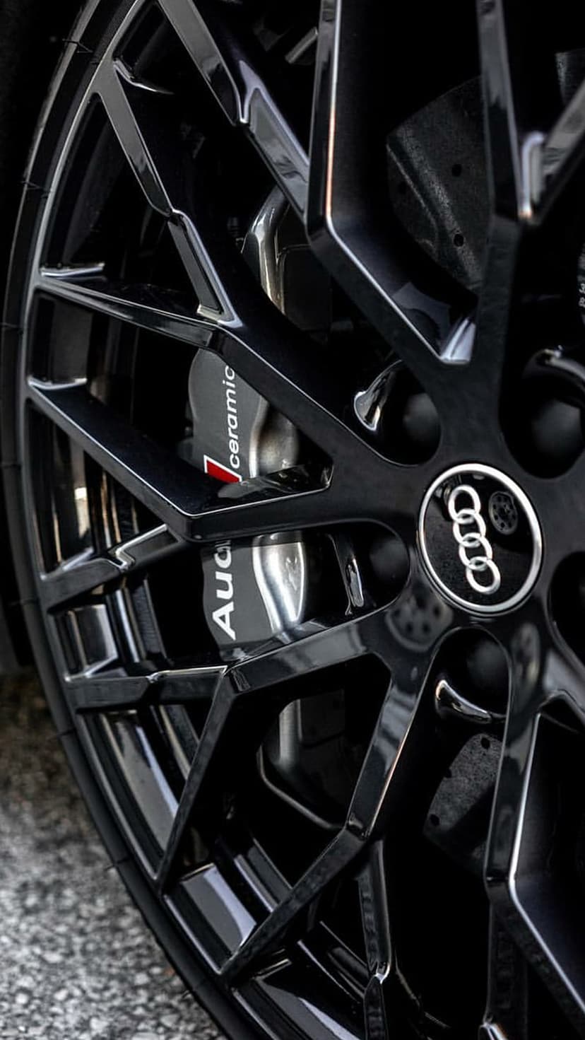 Audi ceramic brake caliper and dark alloy wheel rim displaying intricate mechanical details and glossy textures.