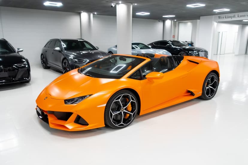 Matte orange Lamborghini Huracán Evo Spyder parked on a white showroom floor among other luxury cars.