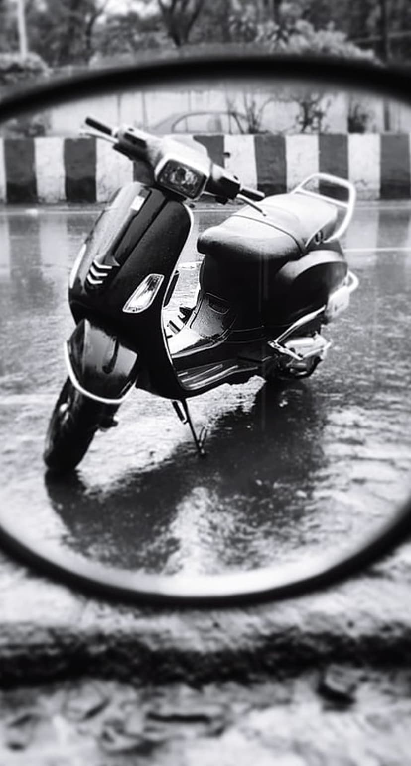 Vintage moped parked on a wet street reflects in a rain puddle with a circular bokeh blur and urban background.