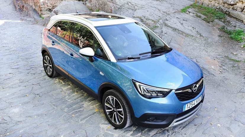 Blue crossover SUV with white roof parked on a grey cobblestone street under soft natural daylight.