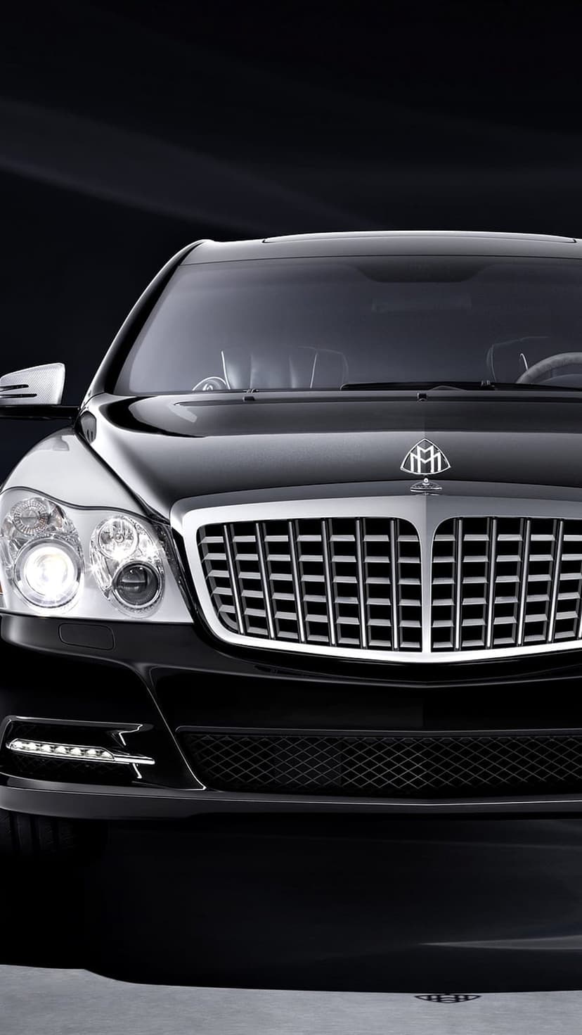 Black Maybach front grille with glowing LED headlights and a silver emblem against a dark, moody background.