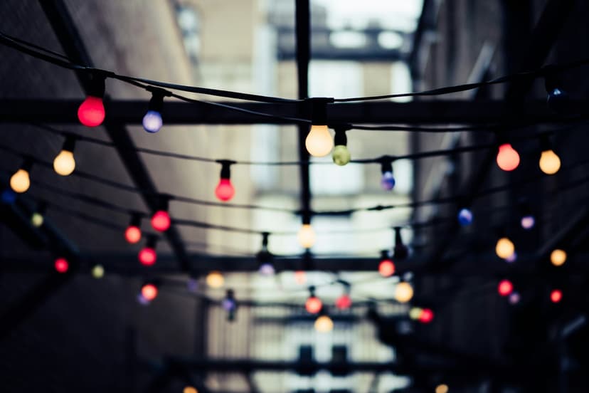 Glowing glass bulbs hang on a string above a darkened alleyway with soft colorful bokeh circles in the background.