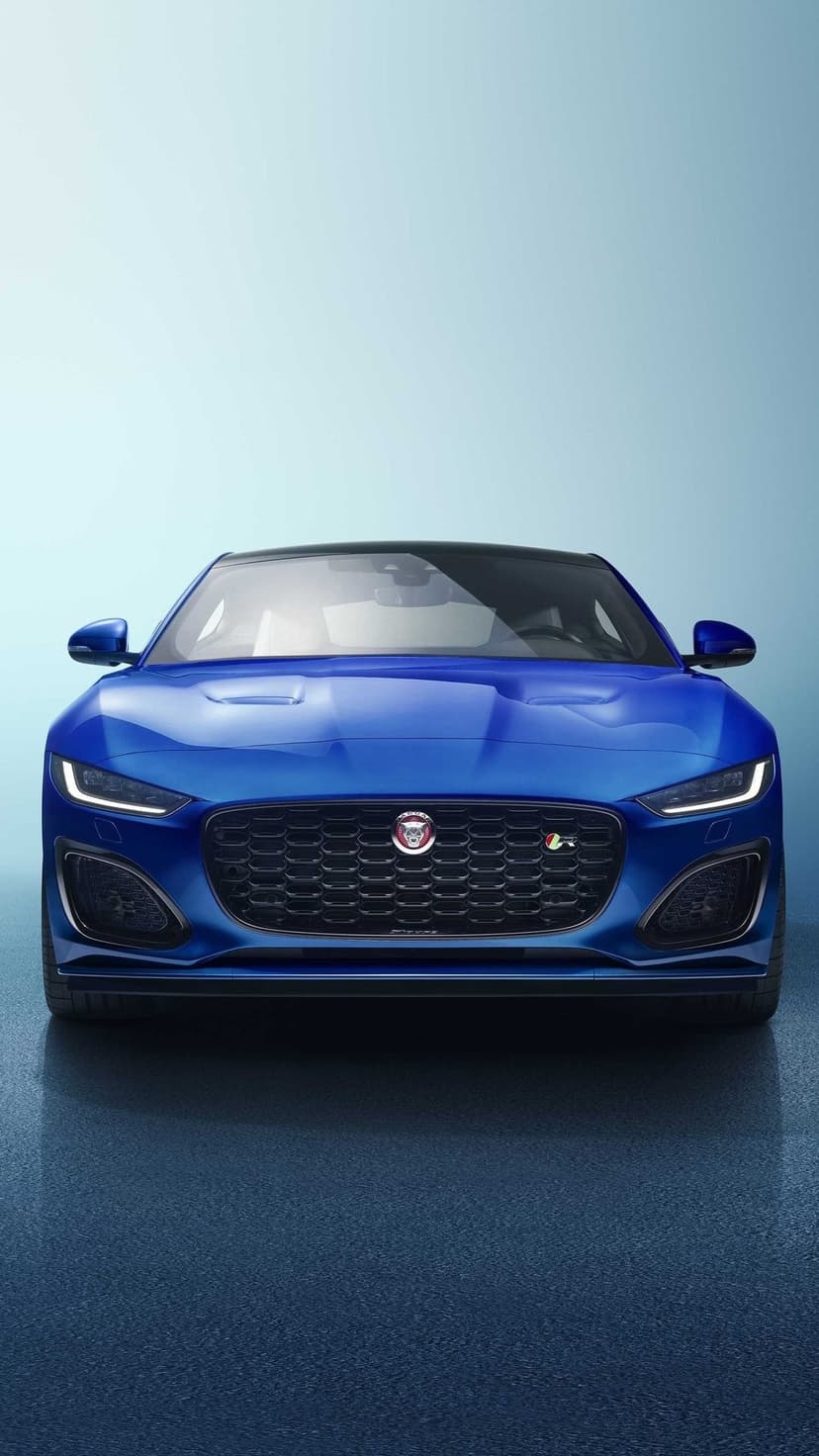 Front view of a blue Jaguar F-Type with glowing LED lights and black grille on a soft blue background.