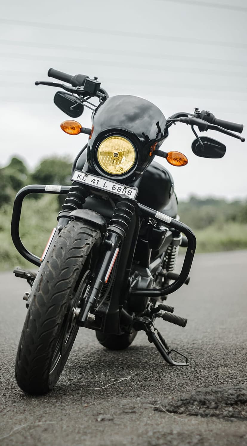 Black Harley-Davidson Street 750 motorcycle with a yellow headlight parked on an asphalt road under cloudy skies.