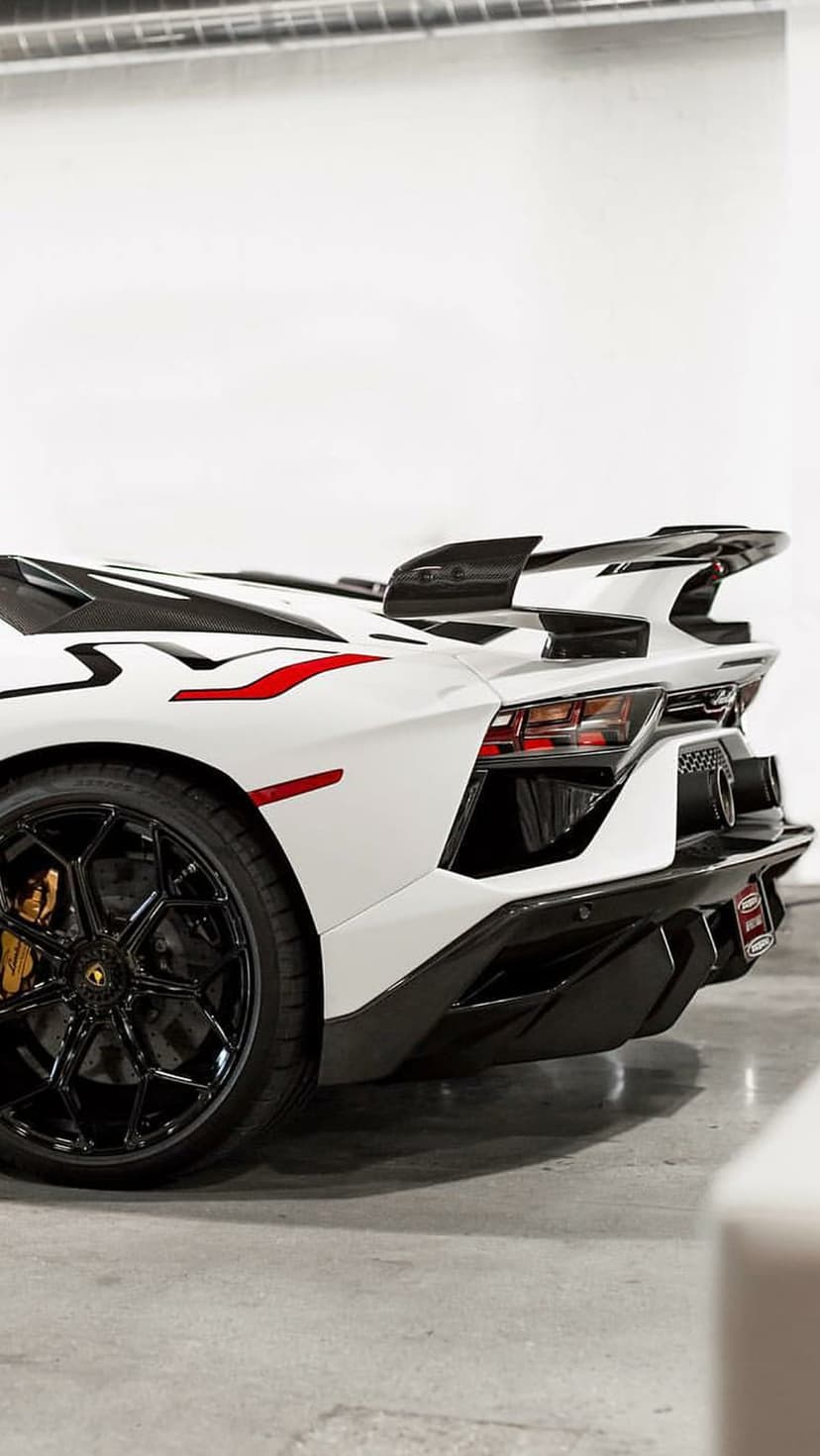 Lamborghini Aventador SVJ rear spoiler with carbon fiber accents, red stripes, and a black wheel with gold calipers.