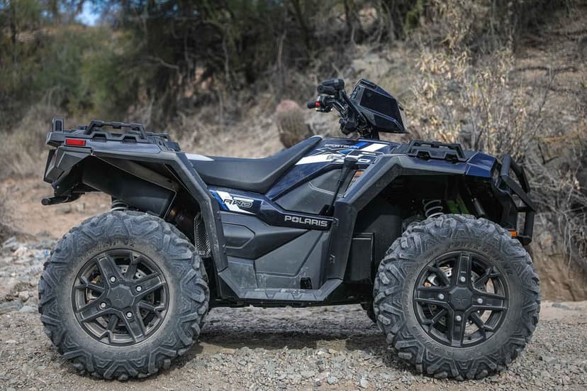 A black Polaris Sportsman XP 1000 ATV parked on a rocky desert trail under bright natural sunlight.