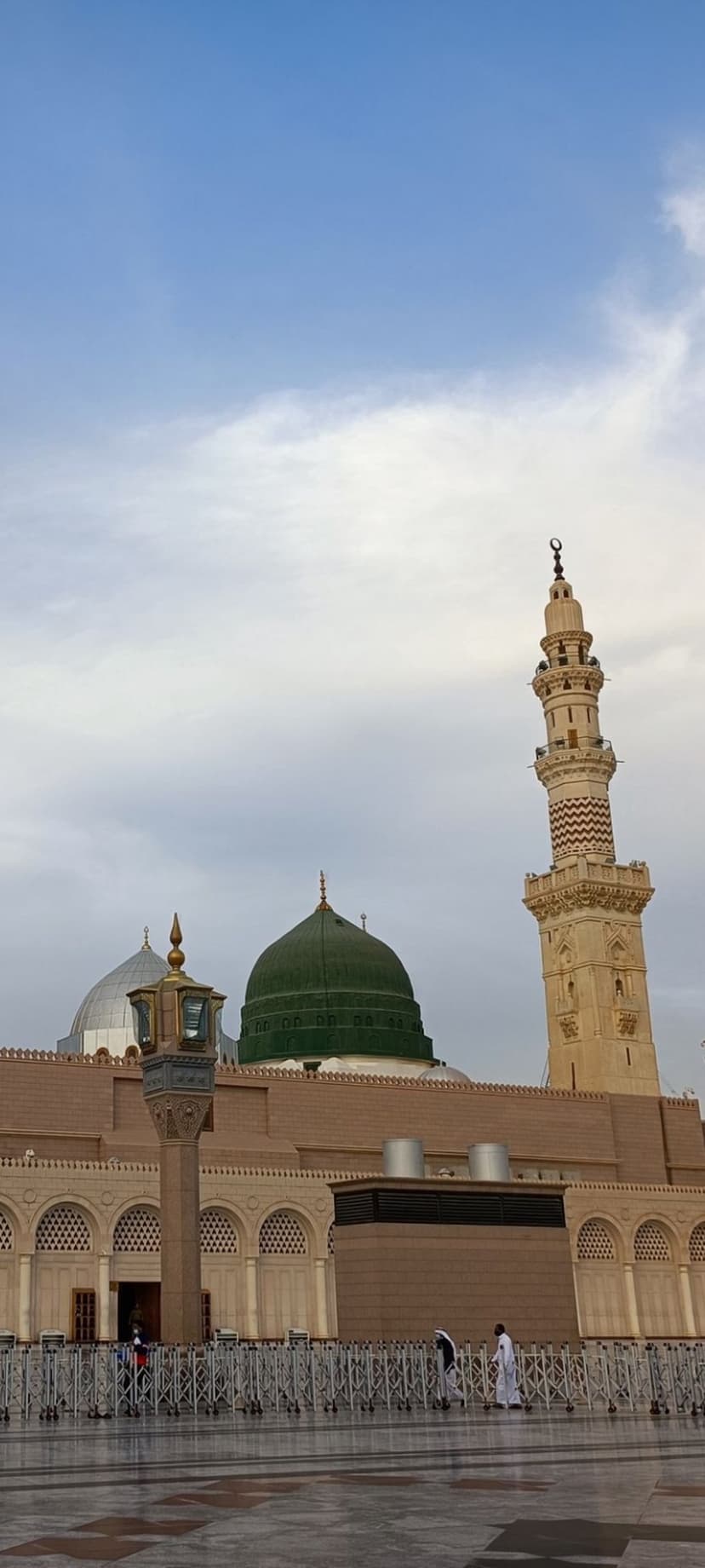 Green Dome of the Prophet's Mosque and a tall minaret under a blue sky with soft clouds in Medina, Saudi Arabia.