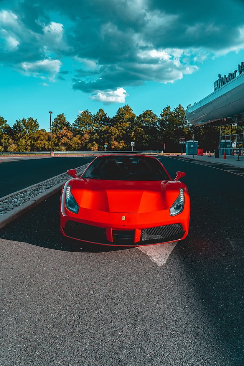 Red Ferrari 488 GTB sports car parked on asphalt before a modern building under a dramatic cloudy sky.