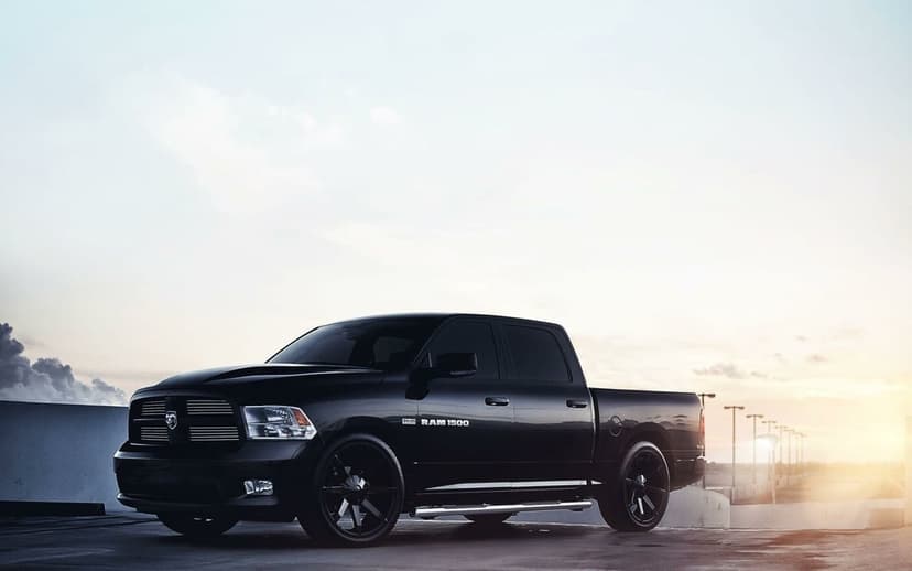 Black Ram 1500 pickup truck with custom wheels parked on a concrete rooftop during a golden hour sunset.