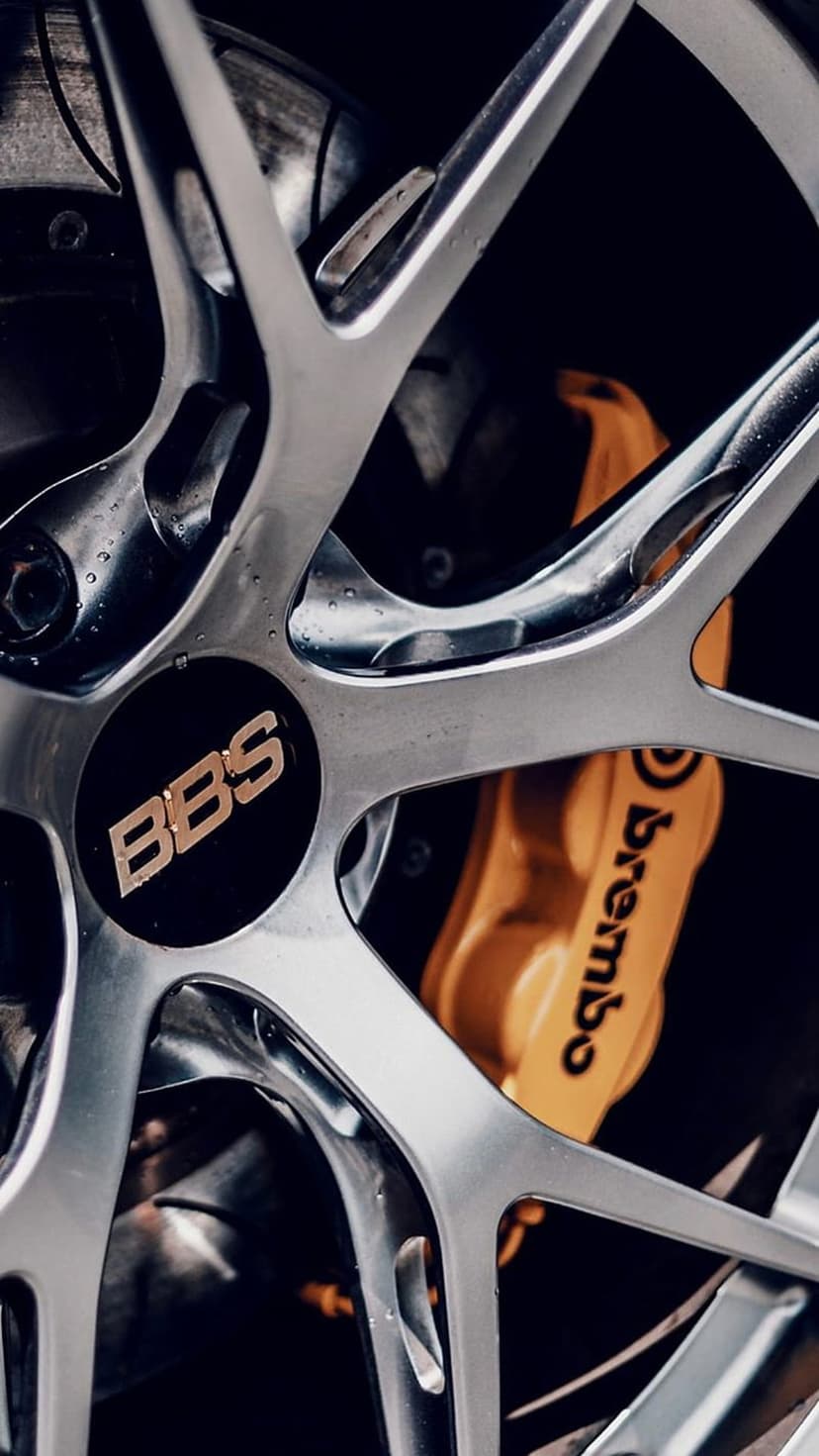 Silver BBS alloy wheel with intricate spokes revealing a gold Brembo brake caliper covered in water droplets.