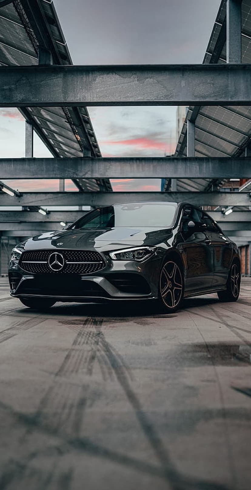 Mercedes-Benz CLA Coupe parked on concrete under industrial solar panels during a dusky pink and gray twilight.
