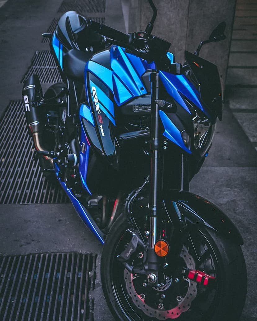 Blue Suzuki GSX-S 750 motorcycle on a metal grate featuring an SC exhaust and sharp front forks in low light.