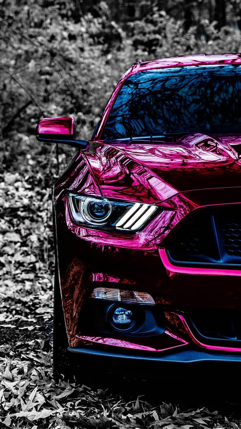 Chrome pink Ford Mustang headlight and mesh grille reflecting a black and white forest on the metallic bodywork.