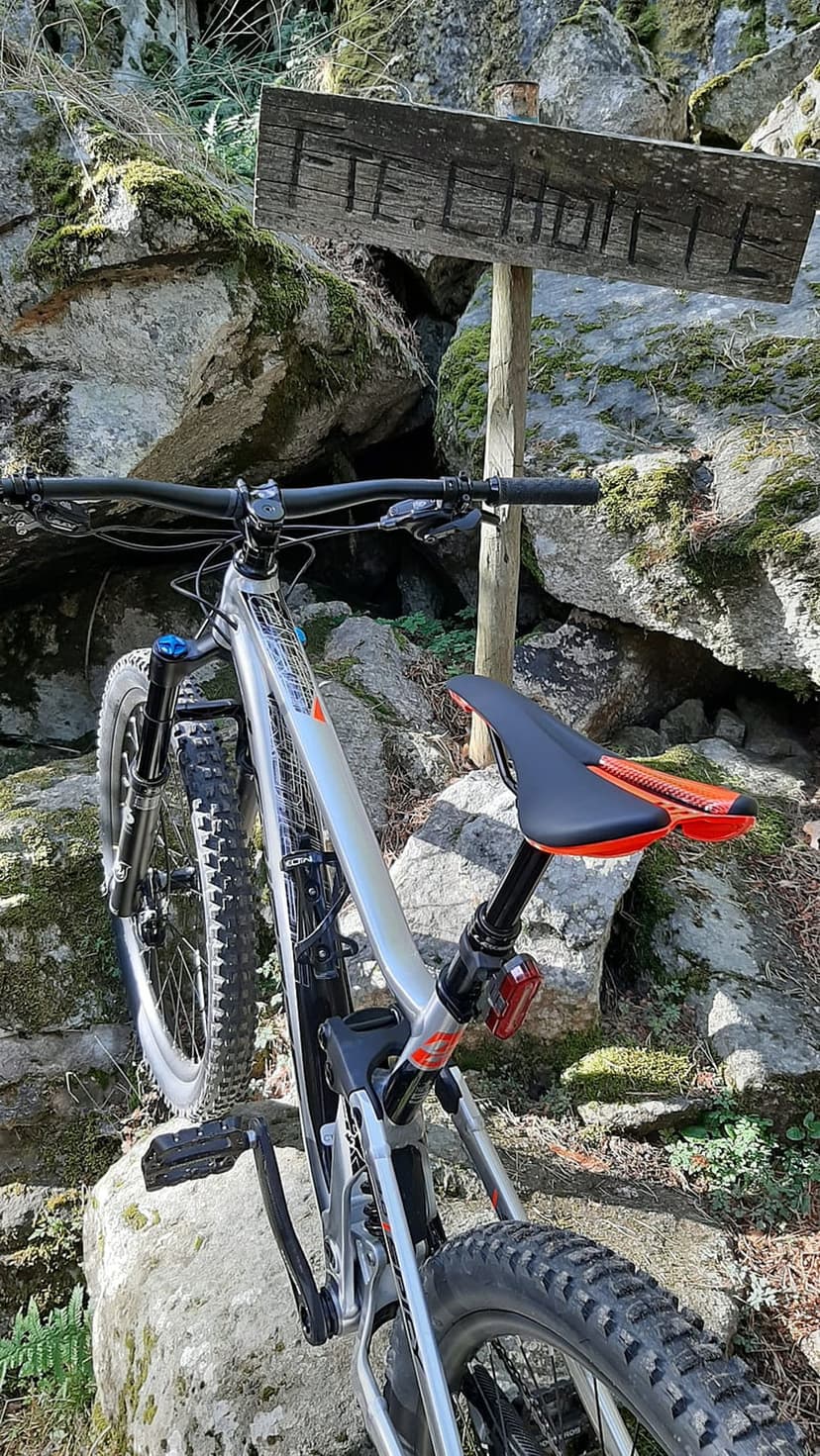 Silver mountain bike with orange accents parked beside a weathered wooden sign on a mossy rocky trail.